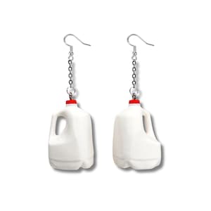 Peut inclure: Paire de boucles d'oreilles fantaisie représentant de petits bidons de lait blancs avec des bouchons rouges. Les boucles sont suspendues à des chaînes et crochets argentés, pour un accessoire original.