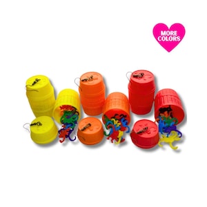 May include: A collection of colorful plastic barrel toys in yellow, orange, and red. Each barrel has a lid and contains small, multi-colored plastic animal figures. The image includes a pink heart with the text "MORE COLORS".
