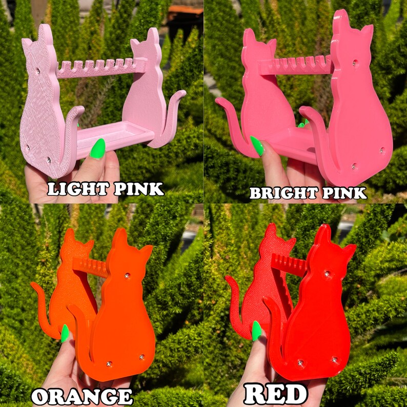 May include: Four cat-shaped wall organizers in different colors: light pink, bright pink, orange, and red. Each organizer has a shelf and a row of hooks for hanging items.