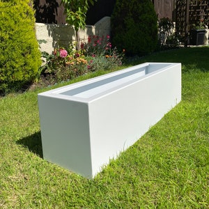 May include: A white rectangular planter made of a smooth material. The planter is sitting on a green lawn.