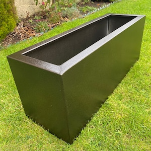 May include: A dark brown rectangular planter made of metal. The planter is sitting on a green lawn.