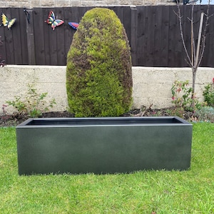 May include: A dark grey rectangular planter made of concrete or a similar material. The planter is sitting on a green lawn.