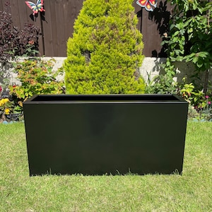 May include: A black rectangular planter sits on a green lawn. The planter is made of metal and has a smooth surface.