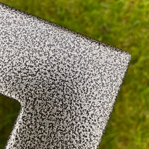 May include: Close-up of a black metal surface with a textured, speckled finish. The surface has a silver-grey color and a rough, uneven texture.