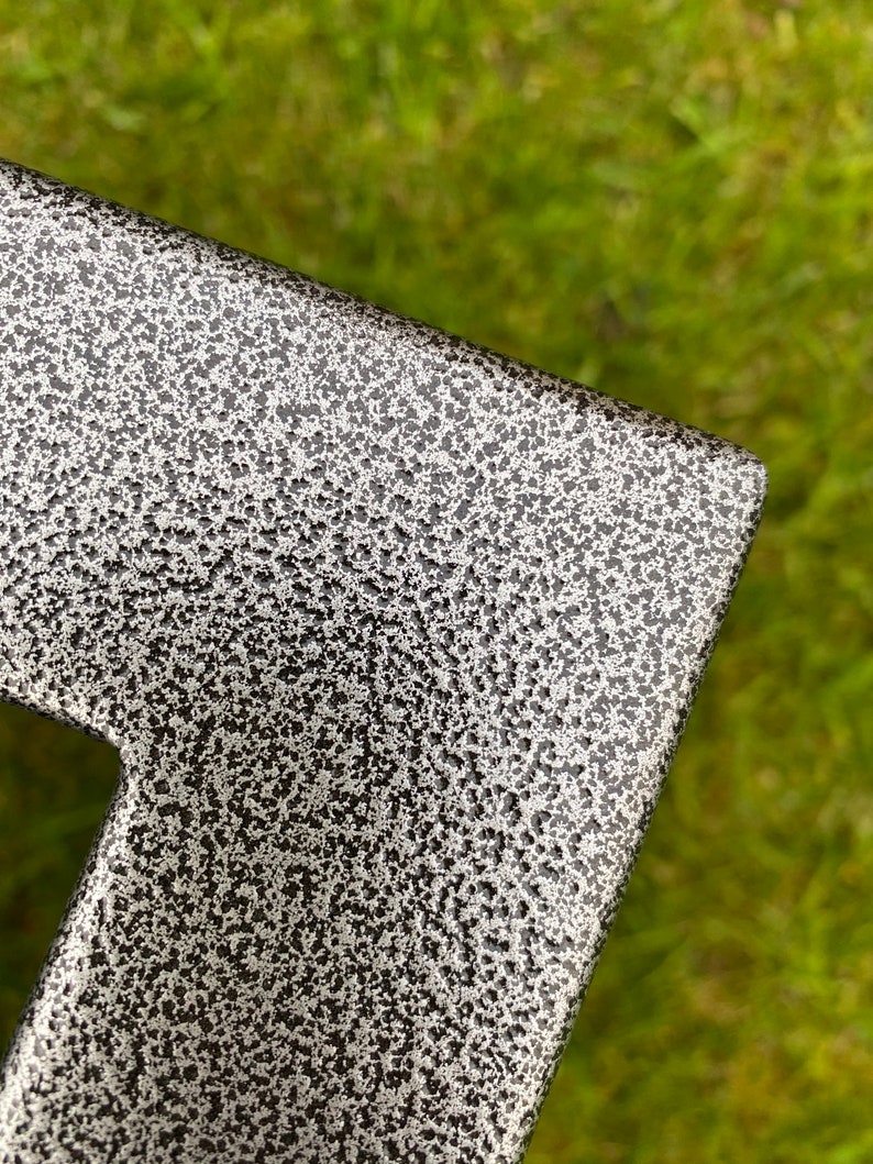 May include: Close-up of a black metal surface with a textured, speckled finish. The surface has a silver-grey color and a rough, uneven texture.
