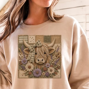 Puede incluir: Una sudadera beige de cuello redondo con un estampado gráfico cuadrado de una vaca Highland con un lazo a cuadros en la cabeza, rodeada por un fondo de patchwork de cuadrados verdes y marrones y un grupo de margaritas y flores moradas.