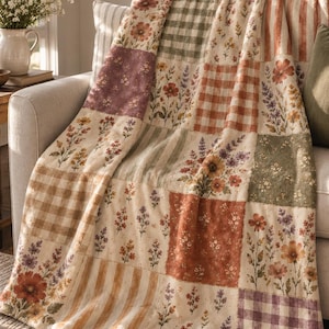 Puede incluir: Una manta de patchwork con un patrón repetitivo de ilustraciones florales, cuadros vichy y rayas verticales en tonos apagados de verde salvia, terracota, crema y lavanda. El tejido muestra una superficie suave y texturizada.