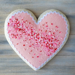 May include: A pink felt heart-shaped cookie with white frosting and pink and red sprinkles.