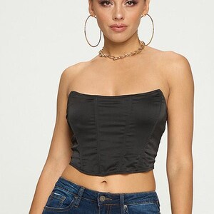May include: A woman is wearing a black strapless top and dark blue skinny jeans. She is wearing gold hoop earrings and a gold chain necklace.
