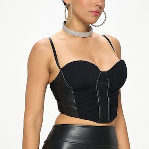 May include: A black faux leather corset top with a sweetheart neckline and a zipper closure. The top has a ruched design and is cropped.