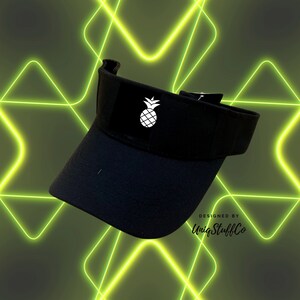 May include: Black visor with a white pineapple graphic and the text "Designed by UniqStuffCo".
