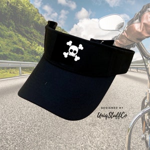 Op de afbeelding: Zwarte visor met een wit schedel- en kruisbeenderontwerp. De visor is ontworpen door UniqStuffCo.