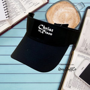 May include: Black visor with a white "Christ is Risen" graphic. The visor is designed by Unig Stuff Co.