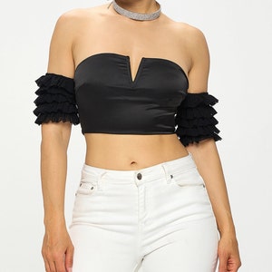 Puede incluir: Un top negro sin hombros, con escote en V y mangas con volantes.