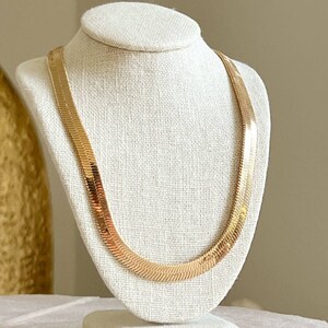 May include: A gold chain necklace with a snake chain design. The necklace is displayed on a white fabric mannequin.