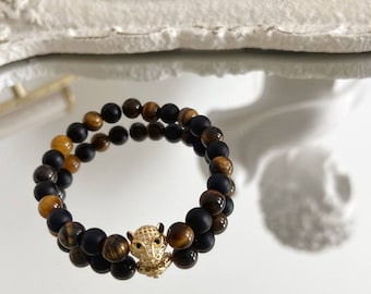 May include: A double-layered bracelet with black and tiger's eye beads. The bracelet has a gold charm in the shape of an owl with a diamond-like design.
