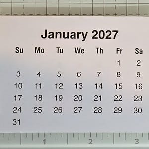 May include: A white paper calendar for January 2027, with the days of the week across the top and dates arranged in a grid. The month and year are in bold black text. The calendar is on a grid.