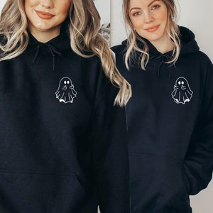May include: Black hooded sweatshirts featuring a white ghost graphic on the chest. The ghost is giving the middle finger. The sweatshirts have a drawstring hood and a front pocket. The sweatshirts are a casual style.