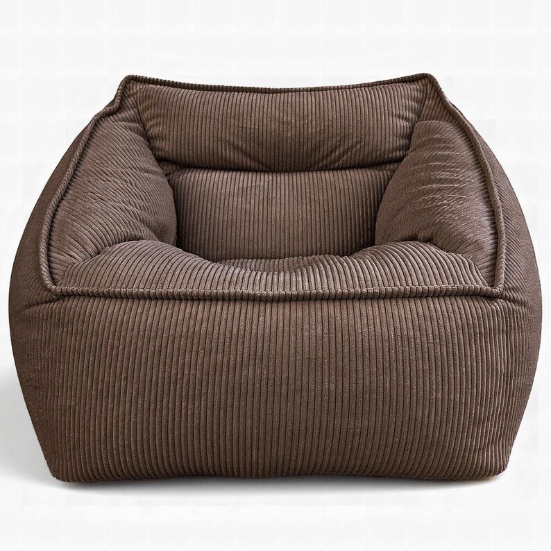 Puede incluir: Un sill&oacute;n bajo de asiento profundo tapizado en tela de pana de color marr&oacute;n oscuro. El sill&oacute;n presenta un respaldo ancho y cuadrado, reposabrazos gruesos y acolchados, y un coj&iacute;n de asiento suave, todo con una textura de canal&eacute; vertical.