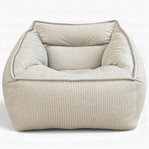 Puede incluir: Un sill&oacute;n bajo de forma cuadrada tapizado en tela de pana de color beige claro. La silla presenta un asiento y respaldo profundos y acolchados con una textura de rayas verticales prominente en toda la superficie exterior.