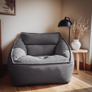 Puede incluir: Un sill&oacute;n de pana gris carb&oacute;n con una silueta suave y redondeada y un respaldo grueso y acolchado. La silla presenta un acabado de tela texturizada y acanalada, junto con un asiento profundo y acolchado para mayor comodidad.