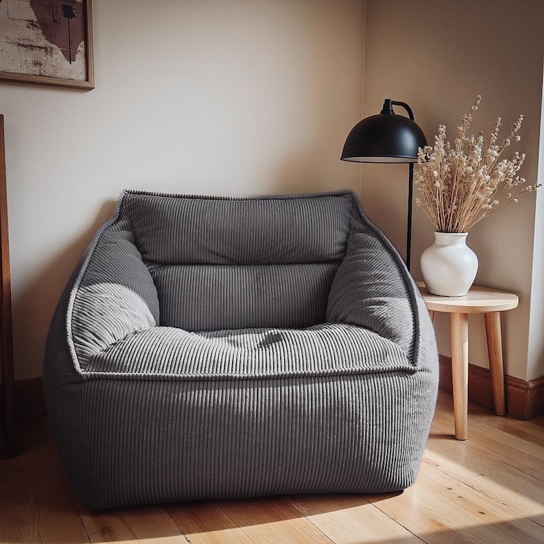 Puede incluir: Un sill&oacute;n de pana gris carb&oacute;n con una silueta suave y redondeada y un respaldo grueso y acolchado. La silla presenta un acabado de tela texturizada y acanalada, junto con un asiento profundo y acolchado para mayor comodidad.