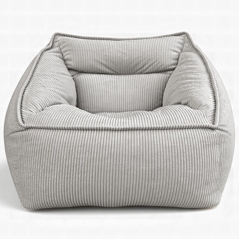 Puede incluir: Un sill&oacute;n de color gris claro tapizado en tela de pana texturizada. La silla presenta un dise&ntilde;o cuadrado de perfil bajo con un asiento profundo, reposabrazos integrados y un respaldo acolchado, todo cubierto con tela de canal&eacute; vertical.
