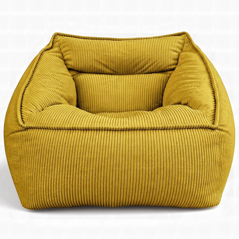 Puede incluir: Un sill&oacute;n de color amarillo mostaza confeccionado en tela de pana texturizada con detalles de acanalado vertical. El sill&oacute;n presenta un dise&ntilde;o cuadrado de perfil bajo con asiento profundo, reposabrazos integrados y respaldo acolchado con costuras visibles.