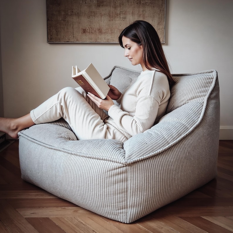 Puede incluir: Un sill&oacute;n lounge de perfil bajo en color gris claro con textura de pana, estructura acolchada suave y bordes ribeteados. El sill&oacute;n cuenta con un asiento profundo y ancho, adem&aacute;s de un respaldo de apoyo para una posici&oacute;n de descanso.