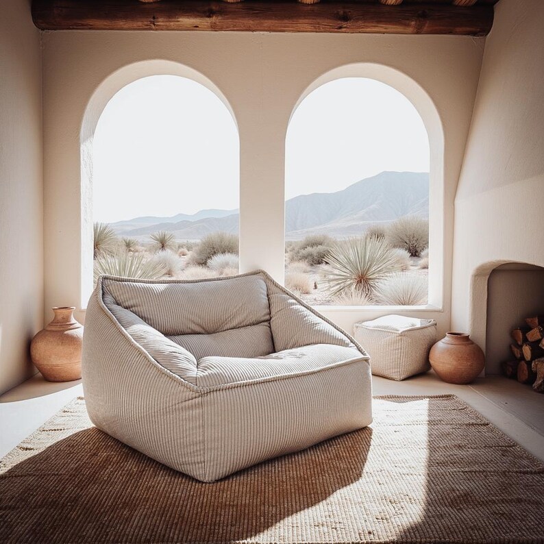 Puede incluir: Un sill&oacute;n bajo de color beige con rayas finas, que cuenta con un asiento y respaldo acolchados. La silla tiene una estructura redondeada y est&aacute; colocada sobre una alfombra tejida, acompa&ntilde;ada de un taburete cuadrado a juego y dos jarrones de terracota.