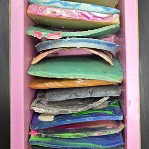 以下が含まれることがあります： ピンク色の長方形の型に、さまざまな色の石鹸バーが詰められています。 石鹸は層状になっており、緑、青、黄色、ピンクなど、さまざまな色を示しています。 各バーには、ユニークなデザインとテクスチャがあります。