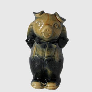 Peut inclure: Une figurine de cochon en céramique portant une tenue bleue et jaune avec un nœud papillon. Le cochon a un groin brun et de grands yeux.