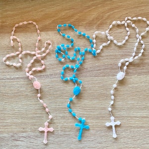 May include: Three plastic rosaries with oval beads and cross charms. One rosary is pink, one is blue, and one is white.