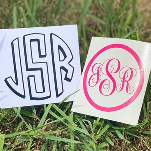 May include: Two white vinyl stickers with black and pink lettering. The first sticker features the letters "JSR" in a bold, blocky font. The second sticker features the letters "JSR" in a cursive font inside a pink circle.