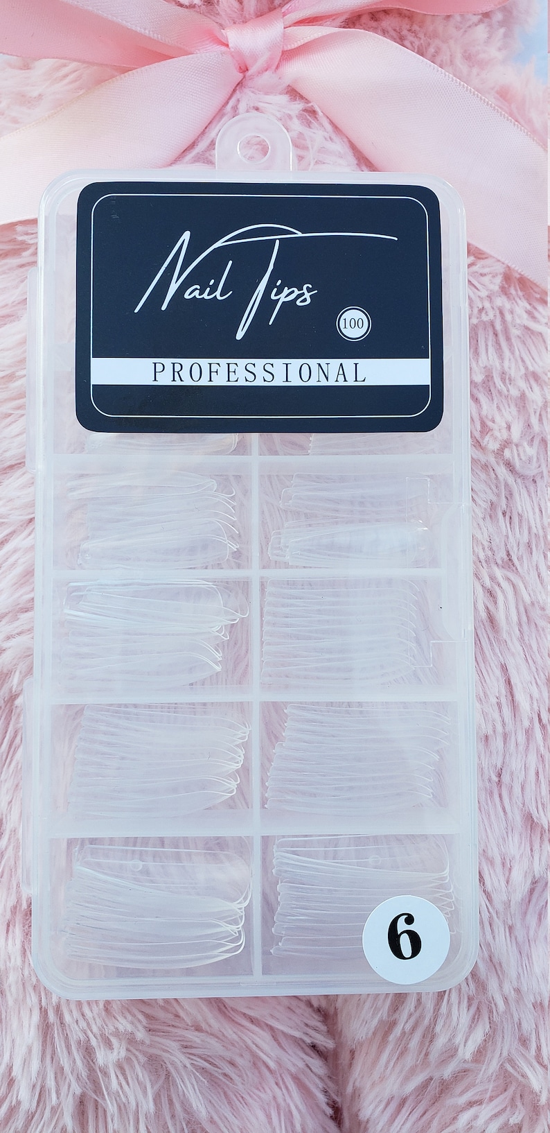 May include: A clear plastic box with a black label that says "Nail Tips Professional (100)". The box contains 6 compartments filled with clear plastic nail tips.