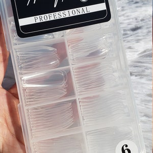 May include: A clear plastic container with 100 clear nail tips in various sizes. The container has a black label that says "Nail Tips Professional 100".