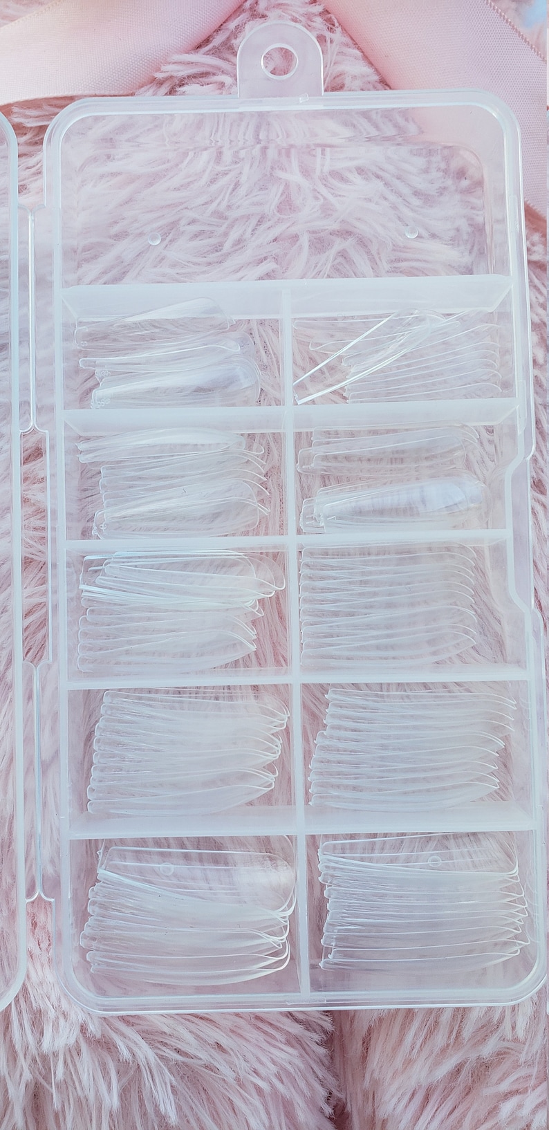 May include: A clear plastic storage box with multiple compartments filled with clear plastic nail tips.