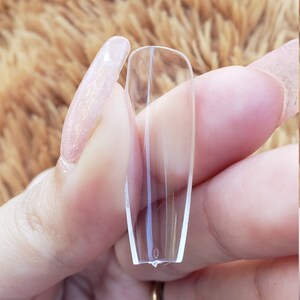 May include: Clear plastic nail tips for nail extensions. The tips are long and narrow, with a slightly curved shape.