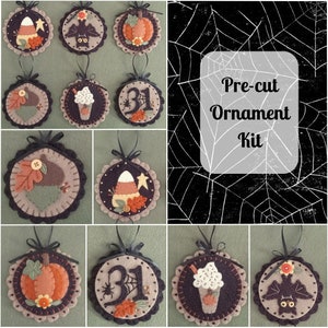 May include: A pre-cut felt ornament kit with a Halloween theme. The kit includes eight ornaments: a pumpkin, a bat, a candy corn, a spider, a coffee cup, a ghost, an acorn, and a number 31.