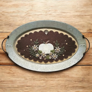 May include: A white pumpkin with brown leaves and white flowers is embroidered on a brown felt oval. The oval is placed on a silver metal oval tray.