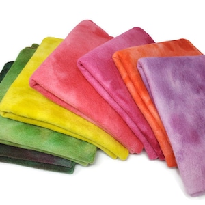 May include: A set of eight folded fabric squares in various shades of green, yellow, orange, pink, and purple. The fabric squares are arranged in a fan shape, with the darkest green square at the bottom and the lightest purple square at the top.