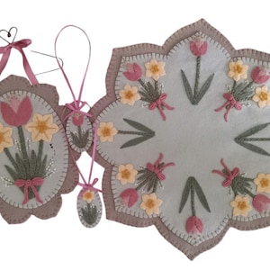 May include: A set of three felt wall hangings featuring embroidered pink tulips and yellow daffodils. The largest hanging is a round, star-shaped piece with a light blue background. The other two hangings are oval shaped with a light gray background.