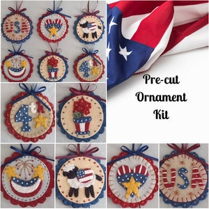 May include: A set of nine felt ornaments with patriotic themes, including a heart, a sheep, a flower pot, fireworks, and the number 4. The ornaments are pre-cut and come in a kit. The text "Pre-cut Ornament Kit" is visible in the image.
