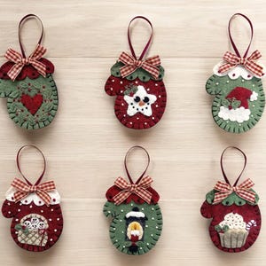 May include: Six felt Christmas ornaments shaped like mittens with different holiday designs. The ornaments are red, green, and white with red and white gingham ribbon.