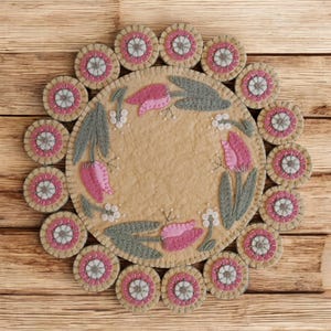 May include: A round felt rug with a floral design featuring pink tulips and green leaves. The rug is surrounded by a border of smaller felt circles with white and pink accents.