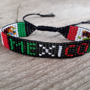 May include: A black beaded bracelet with the word "MEXICO" spelled out in green, white, and red beads. The bracelet also features the colors of the Mexican flag.