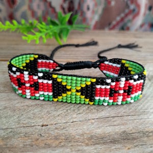 Könnte beinhalten: Ein gewebtes Armband aus Saatperlen mit einem sich wiederholenden geometrischen Muster in leuchtendem Rot, Limettengrün, Schwarz, Weiß und Gelb. Das Armband besteht aus kleinen Glasperlen und hat schwarze Kordelbänder mit verstellbaren Schiebeknoten.