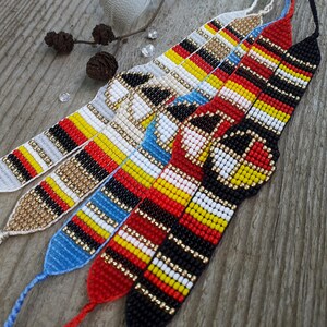 Puede incluir: Cinco pulseras de la amistad con cuentas de varios colores, incluyendo rojo, negro, amarillo, blanco y azul. Las pulseras tienen patrones intrincados y se exhiben sobre una superficie de madera. Cada pulsera mide aproximadamente 18 cm de largo.