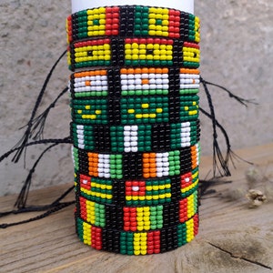May include: A stack of colourful beaded bracelets with black string ties. The bracelets feature a variety of geometric patterns in red, yellow, green, white and black.