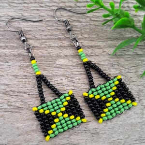 Puede incluir: Pendientes hechos a mano con cuentas que presentan un diseño cuadrado. Los pendientes están hechos con cuentas negras, verdes y amarillas. Tienen una sección superior triangular y una sección inferior cuadrada, con cierre de gancho. Se muestran sobre una superficie de madera.